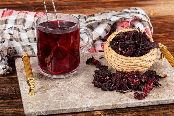 Beyaz ahşap masada, gül yapraklarıyla birlikte cam bardakta kırmızı amber çayı. Hibiscus çay arkaplanı.