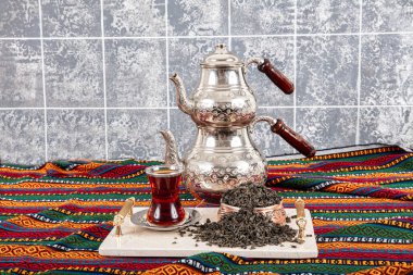 Kurutulmuş siyah çay yaprakları. Çay demleme, çay seremonisi, bir fincan taze demlenmiş siyah çay, karanlık bir ruh hali. Sıcak su, yerel bir masa örtüsü olan bakır çaydanlığın üzerindeki cam bardağa dökülüyor..