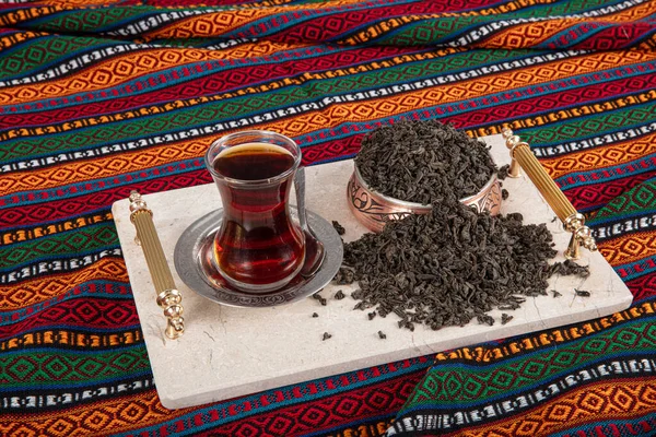 Dried Black tea leaves. Tea brewing, tea ceremony, a cup of freshly brewed black tea, dark mood. Hot water is poured into a glass cup on a copper teapot, local tablecloth.