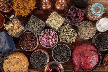 Tahta arka planda sıcak demlenmiş çayla dolu dökme demir çaydanlığın yanında farklı türde yeşil, siyah ve bitkisel çaylar. Lezzetli organik içecekler. Yukarıdan bak.