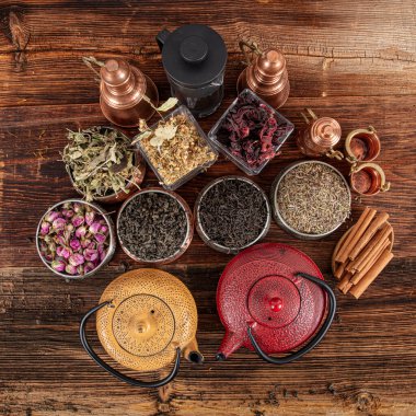 Tahta arka planda sıcak demlenmiş çayla dolu dökme demir çaydanlığın yanında farklı türde yeşil, siyah ve bitkisel çaylar. Lezzetli organik içecekler. Yukarıdan bak.