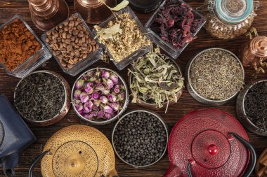 Tahta arka planda sıcak demlenmiş çayla dolu dökme demir çaydanlığın yanında farklı türde yeşil, siyah ve bitkisel çaylar. Lezzetli organik içecekler. Yukarıdan bak.