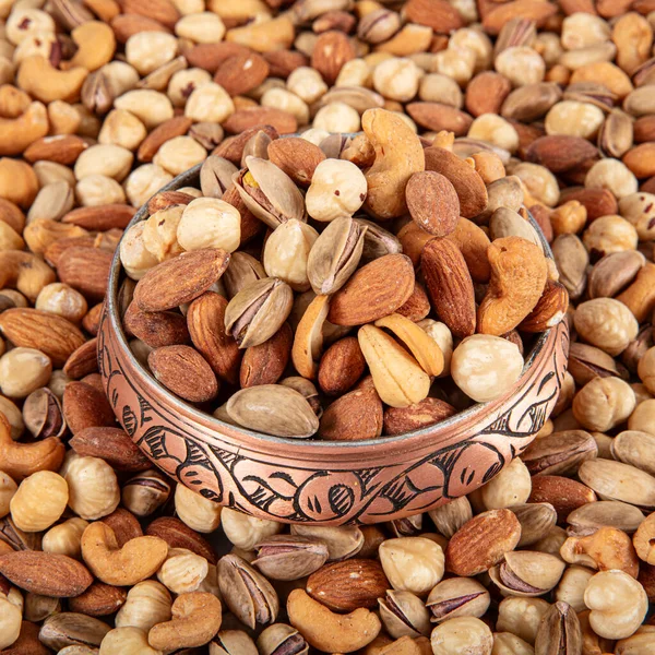 Mixture of dried fruits and nuts in a copper bowl. A mixture of peanuts, pistachios, almonds, hazelnuts and cashews.