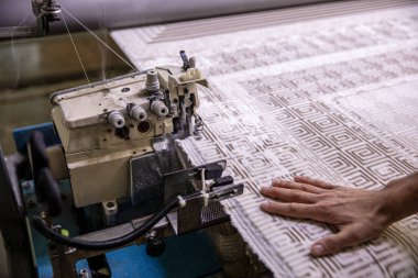 Halı dokuma fabrikasındaki halı kenarı tıkanmış. Endüstriyel dikiş makinesinin halısını diken fabrika işçisi..