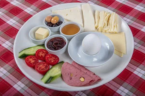 Türk Mutfağı Kahvaltı Tabağı. Dilimlenmiş kiraz domatesli beyaz kahvaltı tabağı, salatalık ve ahşap masada haşlanmış yumurta..