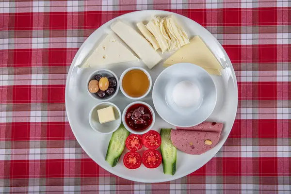 Türk Mutfağı Kahvaltı Tabağı. Dilimlenmiş kiraz domatesli beyaz kahvaltı tabağı, salatalık ve ahşap masada haşlanmış yumurta..