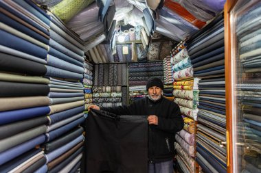 Mardin Türkiye 10 Ocak 2024; Mardin Türkiye 'deki mağaza satıcısı mağaza içinde satılık kumaşı ölçüyor. Kumaş dükkanında mendille çalışan bir satıcı. Küçük İş Konsepti.