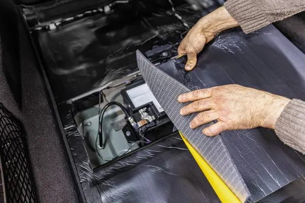 Auto service worker installing soundproofing foam material on car door trim from inside, tuning car sound or installing noise insulation. Process of car sound insulation installation.