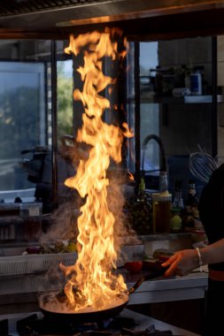 Şef tavada ateş yakar. Aşçı, mutfak sobasında tavada alevle yemek pişiriyor. Restorandaki genç aşçı kızartmada alev saçıyor..