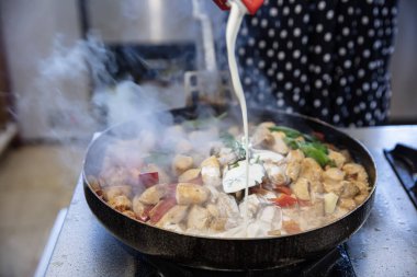 Şef mutfakta kremalı tavuk sote hazırlıyor. Kadın aşçı restoranın mutfağında büyük bir tavada tavuk sote hazırlar..