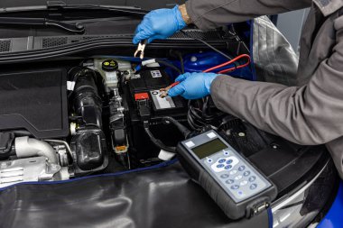 Otomotiv teknisyeni otomatik araç atölyesinde dijital elektronik pil testi ve analizcisi ile otomotiv aküsünü kontrol ve test ediyor..
