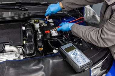 Otomotiv teknisyeni otomatik araç atölyesinde dijital elektronik pil testi ve analizcisi ile otomotiv aküsünü kontrol ve test ediyor..