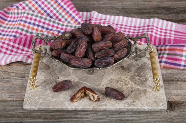 Medina date fruit. Close up shot of date fruit on marble tray in silver bowl on wooden table background. Dried date fruit is healthy as a snack. clipart