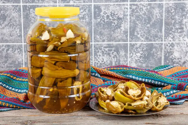 stock image Pickled golden greek peppers, pepperoncino or friggitello (Tuscan, Stavros, Capsicum annuum). Hot peppers are marinated, pickled. Pickled peppers in a plastic jar, Turkish cuisine.