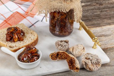 Tahta masada incir reçeli ile düz kompozisyon. Cam kavanozda nefis incir reçeli mermer tepside ve incir reçeli ekmeğin üzerine yayılmış, düz yerde yatıyor..