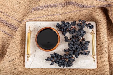 Tahta kasede üzüm pekmezi, tahta kaşıkta kurutulmuş siyah üzüm ve çuval bezi arka planda sağlıklı yiyecek..