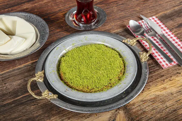 stock image Turkish dessert kunefe, kunafa, kadayif with pistachio powder and cheese, served hot, very sweet. Turkish traditional dessert on wooden background.