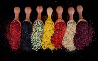 Ahşap kaşıklardaki baharat ve bitkilerden oluşan büyük bir koleksiyon. Siyah arka planda izole edilmiş yiyecek mevsimleri. Renkli bitkiler ve yemek pişirmek için baharatlar. Grafit arka planda bitkiler ve baharatlar.