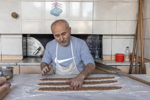 stock image Babadag, Denizli, Turkey March 4, 2024; Baker is baking minced meat pita in a wood-fired oven. Dough, minced meat and vegetables are the ingredients of Turkish pita. Kiymali Pide.