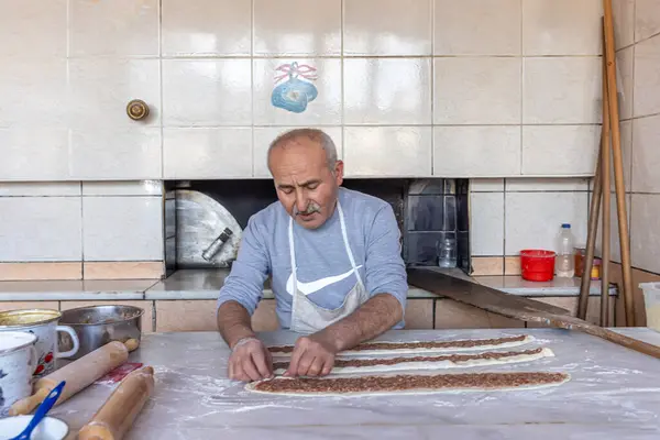 stock image Babadag, Denizli, Turkey March 4, 2024; Baker is baking minced meat pita in a wood-fired oven. Dough, minced meat and vegetables are the ingredients of Turkish pita. Kiymali Pide.