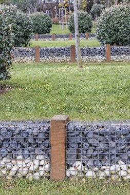 Bahçe düzenlemesi. Doğal bahçe düzeninin karışımı. Dekoratif taşlarla bir duvar örmek peyzaj ve tasarım için tel örgü kullanmak.