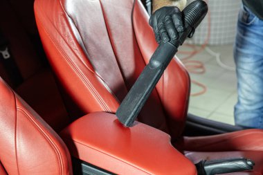 Eldiven takan bir adam deri döşemeli bir arabayı süpürür. İyice temizlik ve bakımını sağlamak için kırmızı deri bir araba koltuğunu süpürmenin detaylı bir görüntüsü.. 