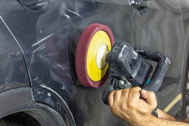 Professional car detailer holds air random orbital sander or dual action polisher in hand while polishing the paint surface of gloss gray paint. Car detail, car wash and paint sealant concept. clipart