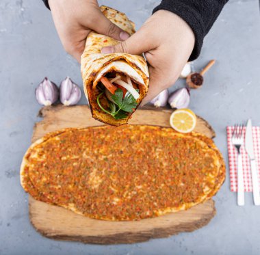 Man's hand holding traditional Turkish dish lahmacun. Turkey famous fast food lahmacun wrapped to be eaten. Turkish Food: lahmacun closeup on a wooden table. clipart