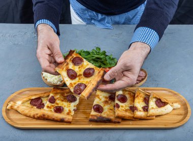 Traditional Turkish Pita; Sucuk Pide. Turkish Pide with Sucuk Sausage, Egg, and Melted Cheese. Young man holding sliced pita bread in his hand. clipart