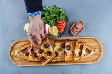 Geleneksel Türk pidesi; Sucuk Pide. Sucuk sosis, yumurta ve erimiş peynirli Türk sandviçi. Elinde dilimlenmiş pita ekmeği tutan genç bir adam..