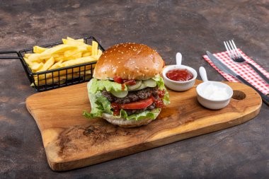 Biftek, soğan, domates, marul ve peynirli ev yapımı lezzetli hamburger. Taze hamburger, ahşap kırsal masada patates kızartmasıyla birlikte. Çizburgermiş. Hamburger..