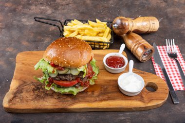 Biftek, soğan, domates, marul ve peynirli ev yapımı lezzetli hamburger. Taze hamburger, ahşap kırsal masada patates kızartmasıyla birlikte. Çizburgermiş. Hamburger..