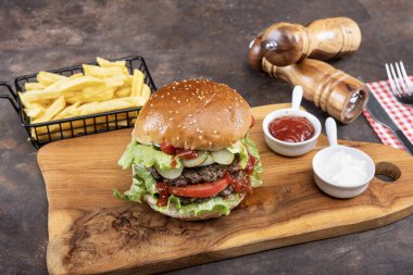 Biftek, soğan, domates, marul ve peynirli ev yapımı lezzetli hamburger. Taze hamburger, ahşap kırsal masada patates kızartmasıyla birlikte. Çizburgermiş. Hamburger..