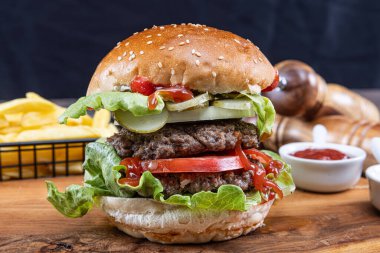 Biftek, soğan, domates, marul ve peynirli ev yapımı lezzetli hamburger. Taze hamburger, ahşap kırsal masada patates kızartmasıyla birlikte. Çizburgermiş. Hamburger..