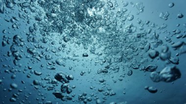 Su altı sanat fotoğrafçılığı. Derin mavi denizde güneş ışığında yüzeye doğru giden hava kabarcıkları..