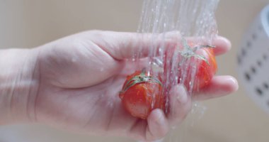 Kadın ellerini kapat ve mutfakta temiz suyla taze kırmızı domatesleri iyice yıka.