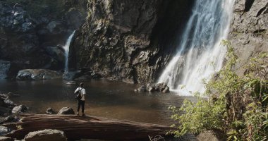 Ayakta duran genç turist Klong Lan Ulusal Parkı 'ndaki Khlong Lan Şelalesinin tadını çıkarıyor. Kamphaeng Phet, Tayland' da güzel bir şelale. Seyahat doğası.