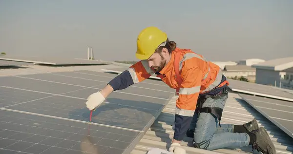 engineer Technician in safety gear installs solar panels on a roof under a clear sky, with a clipboard and tools nearby