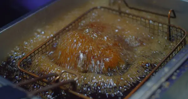 Close-up of chicken deep frying in oil, bubbles simmering in a stainless steel deep fryer