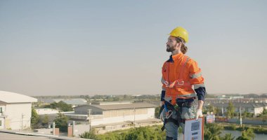 Elinde pano olan bir güneş teknisyeni çatıdaki güneş panellerini inceliyor.