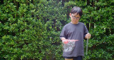 Mutlu, genç Asyalı çocuk gülümseyerek baloncuklu sabun oyuncağı havada sallanırken arka bahçedeki yeşil bahçeye karşı yavaş çekimde, yaz tatili eğlencesi çocukluğunda eğleniyor.