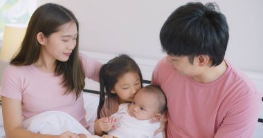 Mutlu Asyalı aile babası anne kızı kucaklaşır birlikte gülümser evde beyaz yatakta uzanır mutlu ebeveyn ve çocuk kız yatak odasında oynaşıp eğlenir