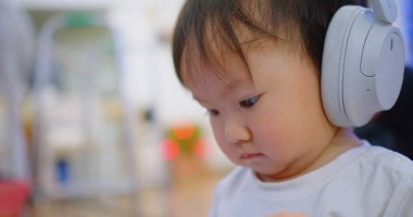 Ciddi bir ifade takınan, beyaz kulaklık takan, kapalı bir arka planda bulanık duran, modern çocukluk ve teknoloji etkileşimini vurgulayan bir çocuğun yakın çekimi..