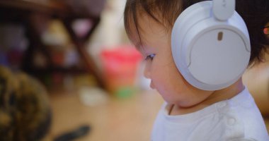 Ciddi bir ifade takınan, beyaz kulaklık takan, kapalı bir arka planda bulanık duran, modern çocukluk ve teknoloji etkileşimini vurgulayan bir çocuğun yakın çekimi..