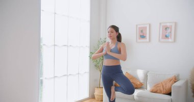 Genç Güzel Kadın Egzersizleri Ağaç Yoga Pozu 'nda denge kurarken evde yoga yaparken, sağlıklı yaşam tarzını, zindeliği, refahı ve farkındalığı artırıyor.