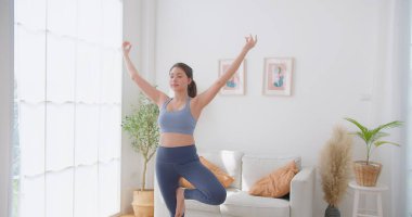 Genç Güzel Kadın Egzersizleri Ağaç Yoga Pozu 'nda denge kurarken evde yoga yaparken, sağlıklı yaşam tarzını, zindeliği, refahı ve farkındalığı artırıyor.