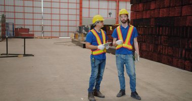 Üniformalı güvenlik ve tablet tutan işçi ortakları Metal İnşaat Üretim Fabrikası 'ndaki bir toplantıda konuşurken mühendisler endüstriyel projeleri tartışıyor. Takım çalışması.