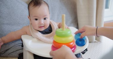 Neşeli bebek sandalyeye oturur ve annesinin yardımıyla renkli yüzükler takmayı öğrenir. Çocukluk gelişimi aktiviteleriyle meşgul olan bir an..