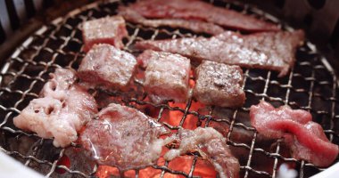 Sulu çiğ et dilimleri kömür ızgarasında barbekü bifteği, alev dumanı, Japon usulü yakiniku barbekü ızgarası.