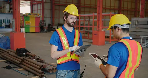 Workers partners in uniform safety and hardhat holding tablet Talking on a Meeting in Metal Construction Manufacture industry factory, Engineers man industrial discussing project work. Team work